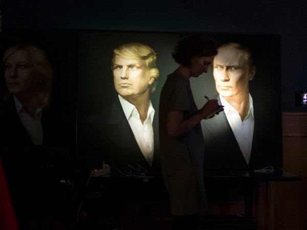 A journalist  writes a material as she watches a live telecast of the U.S. presidential election standing at portraits of Hillary Clinton, Donald Trump and Vladimir Putin in the Union Jack pub in Moscow, Russia, Wednesday, Nov. 9, 2016. Russia's lower house of parliament is applauding the election of Donald Trump as U.S. president. (AP Photo/Alexander Zemlianichenko)