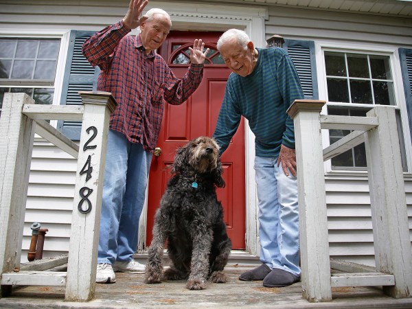 HOLD FOR EARLY RISER SUNDAY JULY 2, 2017 WITH STORY BY DAVID SHARP - In this Friday, June 30, 2017 photo 86-year-old Richard Prekins, right, Robert Maurais and their labradoodle "Scamp" outside their home in Ogunquit, Maine. Politicians have been chipping away at funding for heating aid to low-income Americans for a decade. Now President Donald Trump has proposed ending it altogether, eliciting an outcry from low-income residents who depend on the program to stay warm. (AP Photo/Stephan Savoia)