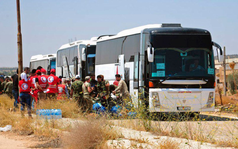 In this photo released by the Syrian official news agency SANA, ﻿Syrian government forces and Syrian Arab Red Crescent oversee the evacuation by buses of opposition fighters and their families from the southern province of Daraa, Syria, Sunday, July 15, 2018. The evacuation deal will hand over areas held by the rebels for years back to government control. Daraa, which lies on a highway linking Damascus with Jordan, was the cradle of the 2011 uprising against Syrian President Bashar Assad. (SANA via AP)