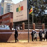 A portrait of Zimbabwean President Emmerson Mnangagawa is seen at the party headquarters as police  walk past the Zimbabwe Electoral Commission offices after  they blocked dozens of opposition party supporters  from entering the  commission offices in  Harare,  Zimbabwe,Wednesday, Aug, 1, 2018. Zimbabweans are awaiting the  first results from an election that they hope will lift the country out of economic and poltical stagnation  after decades of  rule by former leader Robert Mugabe (AP Photo/Tsvangirayi Mukwazhi)