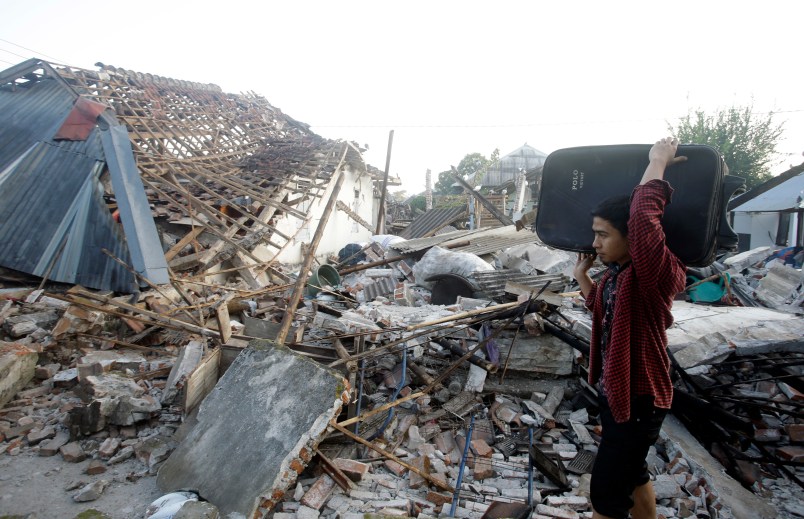 A man carries his belonging pass ruin houses at a village affected by Sunday's earthquake in North Lombok, Indonesia, Thursday, Aug. 9, 2018. The north of Lombok has been devastated by the magnitude 7.0 quake that struck Sunday night, damaging thousands of buildings and killing a large number of people. (AP Photo/Firdia Lisnawati)