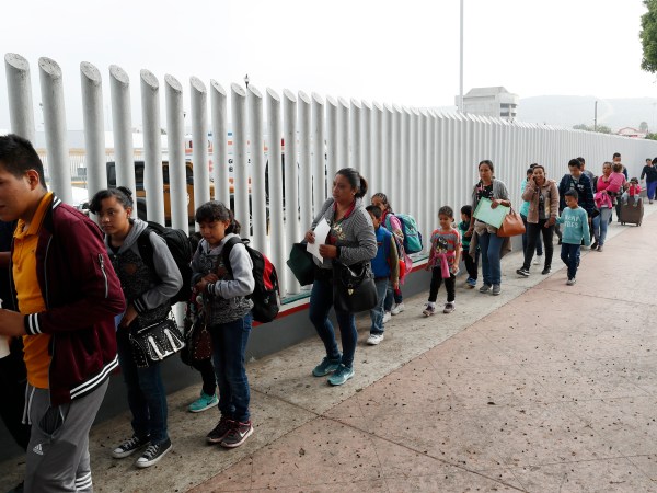 FILE. This July 26, 2018 file photo shows people lining up to cross into the United States to begin the process of applying for asylum near the San Ysidro port of entry in Tijuana, Mexico.A federal judge has extended a freeze on deporting families separated at the U.S.-Mexico border, giving a reprieve to hundreds of children and their parents to remain in the United States.(AP Photo/Gregory Bull, File)