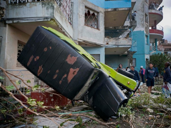 People walk next to a car overturned by the force of the tornado in Havana, Cuba, Monday, Jan. 28, 2019. A tornado and pounding rains smashed into the eastern part of Cuba's capital overnight, toppling trees, bending power poles and flinging shards of metal roofing through the air as the storm cut a path of destruction across eastern Habana.Power was cut to many areas and President Miguel Diaz-Canel said Monday at least three people were killed and 172 injured. (AP Photo/Ramon Espinosa)