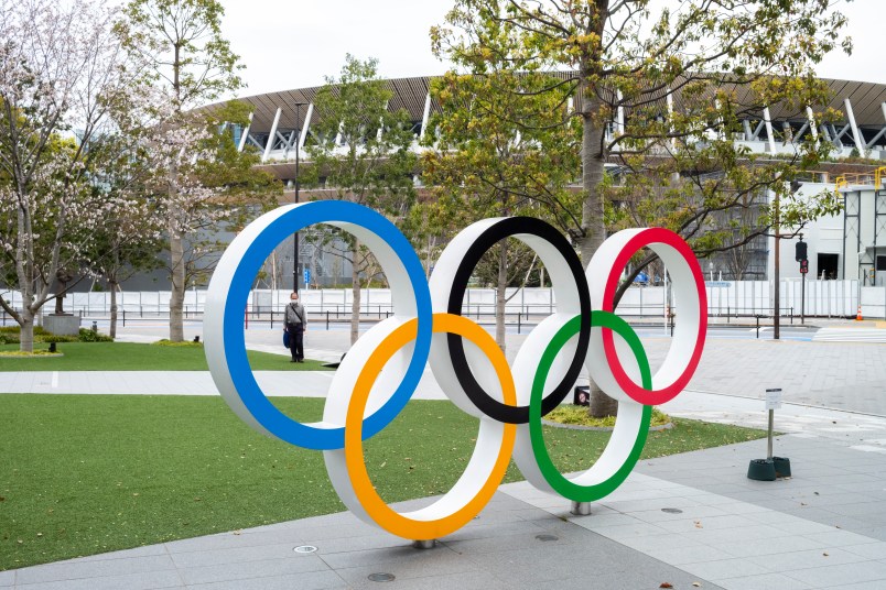 TOKYO, JAPAN, MARCH 27TH 2020 - Am man wearing protective mask stands by the Olympic logo at the new National Stadium built for the 2020 Olympics that have just be posponed to 2021 due to coronavirus outbreak