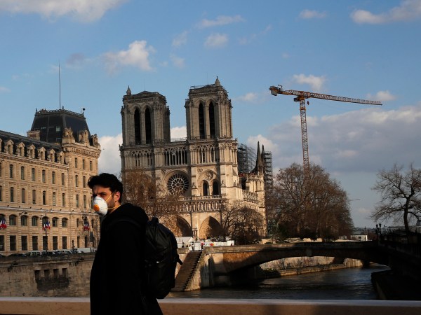 A masked man walks next to Notre Dame Cathedral, in Paris, Wednesday, March 18, 2020. French President Emmanuel Macron said that for 15 days people will be allowed to leave the place they live only for necessary activities such as shopping for food, going to work or taking a walk. For most people, the new coronavirus causes only mild or moderate symptoms. For some it can cause more severe illness, especially in older adults and people with existing health problems. (AP Photo/Francois Mori)