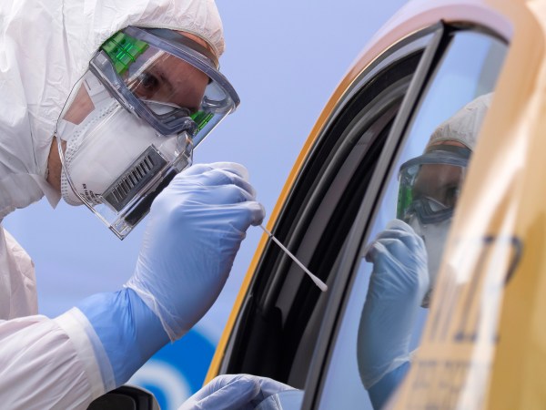 A helper of the German Red Cross DRK in protective suit, left, takes a smear from a patient in his car during the official opening of a drive-through (drive-in) COVID-19 testing center at the fair ground in Dresden, eastern Germany, Wednesday, April 15, 2020. The appointment-only drive-through testing center is starting today with working. Medical staff reache into a car to take a nasopharyngeal swab from a patient. (AP Photo/Jens Meyer)