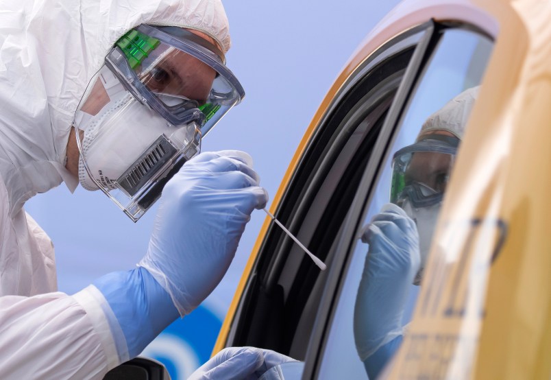 A helper of the German Red Cross DRK in protective suit, left, takes a smear from a patient in his car during the official opening of a drive-through (drive-in) COVID-19 testing center at the fair ground in Dresden, eastern Germany, Wednesday, April 15, 2020. The appointment-only drive-through testing center is starting today with working. Medical staff reache into a car to take a nasopharyngeal swab from a patient. (AP Photo/Jens Meyer)