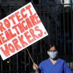 Doctor Meenal Viz holds a banner as she protests outside Downing Street in London, as the country is in lockdown to help curb the spread of the coronavirus, Sunday, April 19, 2020. The doctor who is pregnant was protesting about the lack of PPE and protection for NHS health workers. (AP Photo/Kirsty Wigglesworth)