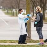 Milwaukee, WI - APRIL 7th: A woman hands out surgical masks to people standing in line to vote in Wisconsin’s spring primary election on Tuesday April 7th, 2020 at Riverside High School in Milwaukee, WI. (Photo by Sara Stathas for the Washington Post)