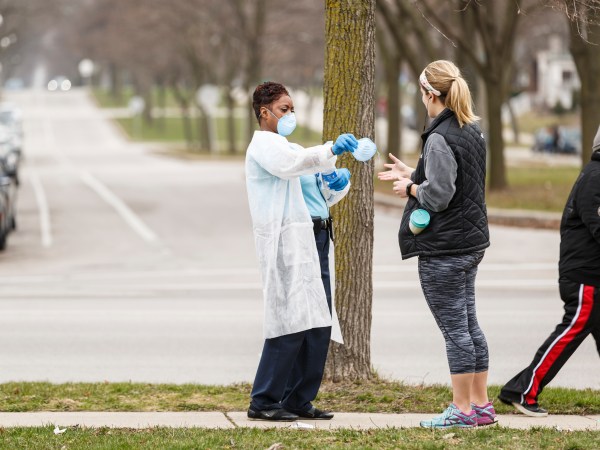 Milwaukee, WI - APRIL 7th: A woman hands out surgical masks to people standing in line to vote in Wisconsin’s spring primary election on Tuesday April 7th, 2020 at Riverside High School in Milwaukee, WI. (Photo by Sara Stathas for the Washington Post)