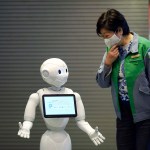 A humanoid robot Pepper with a face mask  greets Tokyo Gov. Yuriko Koike at the lobby of a hotel for the new coronavirus COVID-19 patients with mild symptoms during a media preview in Tokyo Friday, May 1, 2020. Prime Minister Shinzo Abe said Thursday he planned to extend a state of emergency beyond the scheduled end of May 6 because infections are spreading and hospitals are overburdened. (AP Photo/Eugene Hoshiko)