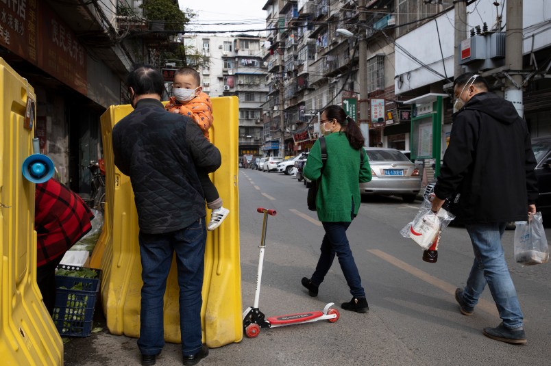 In this photo taken Wednesday, April 1, 2020, residents walk past a sealed off neighborhood in Wuhan in central China's Hubei province. Authorities in Wuhan, the Chinese city where the coronavirus pandemic first broke out, have reportedly launched a plan to test everyone in the city of 11 million people in the next 10 days.  (AP Photo/Ng Han Guan)