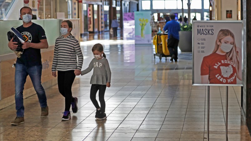 Shoppers walks past a sign encouraging masks at SouthPark Mall, Wednesday, May 13, 2020, in Strongsville, Ohio. Ohio retail businesses reopened Tuesday following a nearly two-month-long shutdown ordered by Gov. Mike DeWine to limit the spread of the coronavirus.  (AP Photo/Tony Dejak)