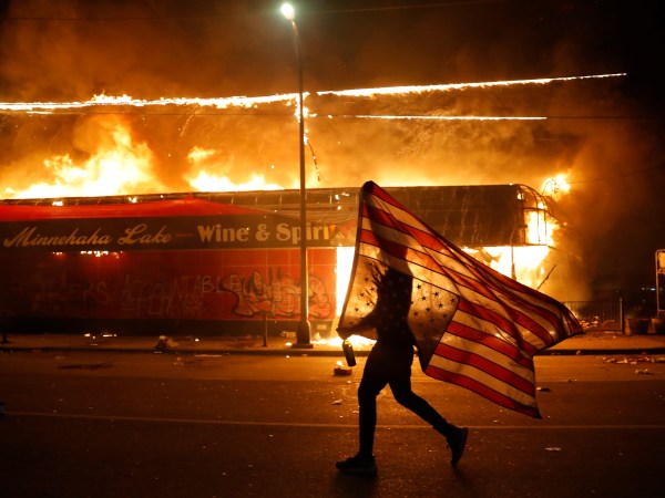 A protester carries the carries the U.S. flag upside, a sign of distress, Thursday, May 28, 2020, in Minneapolis. Violent protests over the death of George Floyd, the black man who died in police custody broke out in Minneapolis for a third straight night. (AP Photo/Julio Cortez)