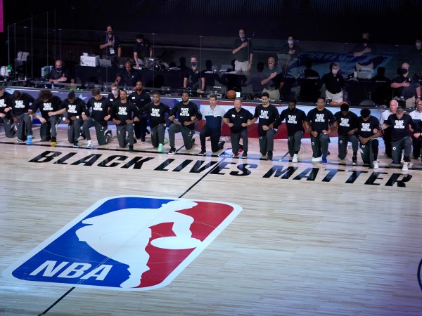 Members of the Milwaukee Bucks and the Boston Celtics kneel around a Black Lives Matter logo before the start of an NBA basketball game Friday, July 31, 2020, in Lake Buena Vista, Fla. (AP Photo/Ashley Landis, Pool)