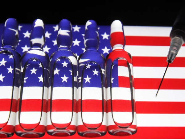 UKRAINE - 2020/11/13: In this photo illustration a syringe and  ampules with fake COVID-19 vaccine seen with the U.S flag in the background. (Photo Illustration by Pavlo Conchar/SOPA Images/LightRocket via Getty Images)
