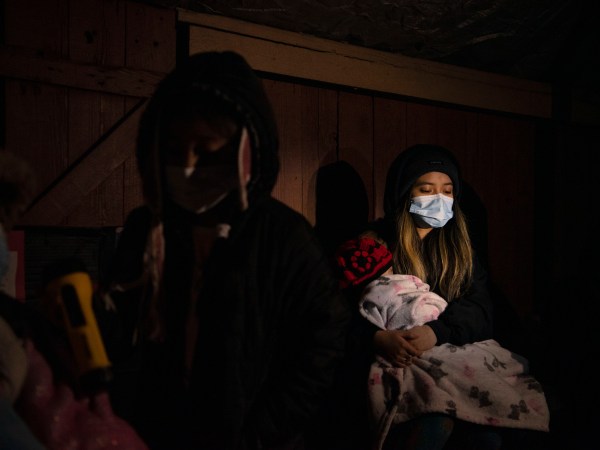 HOUSTON, TX - FEBRUARY 18: Surrounded by tarp and bedsheets, Evelyn Hernandez, 15, and her sister, Daeslyn Hernandez, 1, keep warm by the glow of a camping stove on their family’s front porch following an unprecedented winter storm in Houston, Texas on February 18, 2021. The Hernandez family lost power on Monday morning and are preparing for another deep freeze.  (Photo by Callaghan O’Hare for The Washington Post)