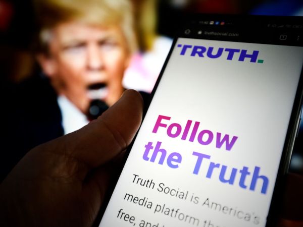The TRUTH Social website is seen on a mobile device with an image of former US president Donald Trump in the background in this photo illustration in Warsaw, Poland on 23 February, 2022. TRUTH Social is a newly developed social media platform by the Trump Media and Technology Group (TMTG) modelled after Twitter. The initiative was taken after Trump himself had been banned from Facebook and Twitter in 2021. (Photo by STR/NurPhoto)